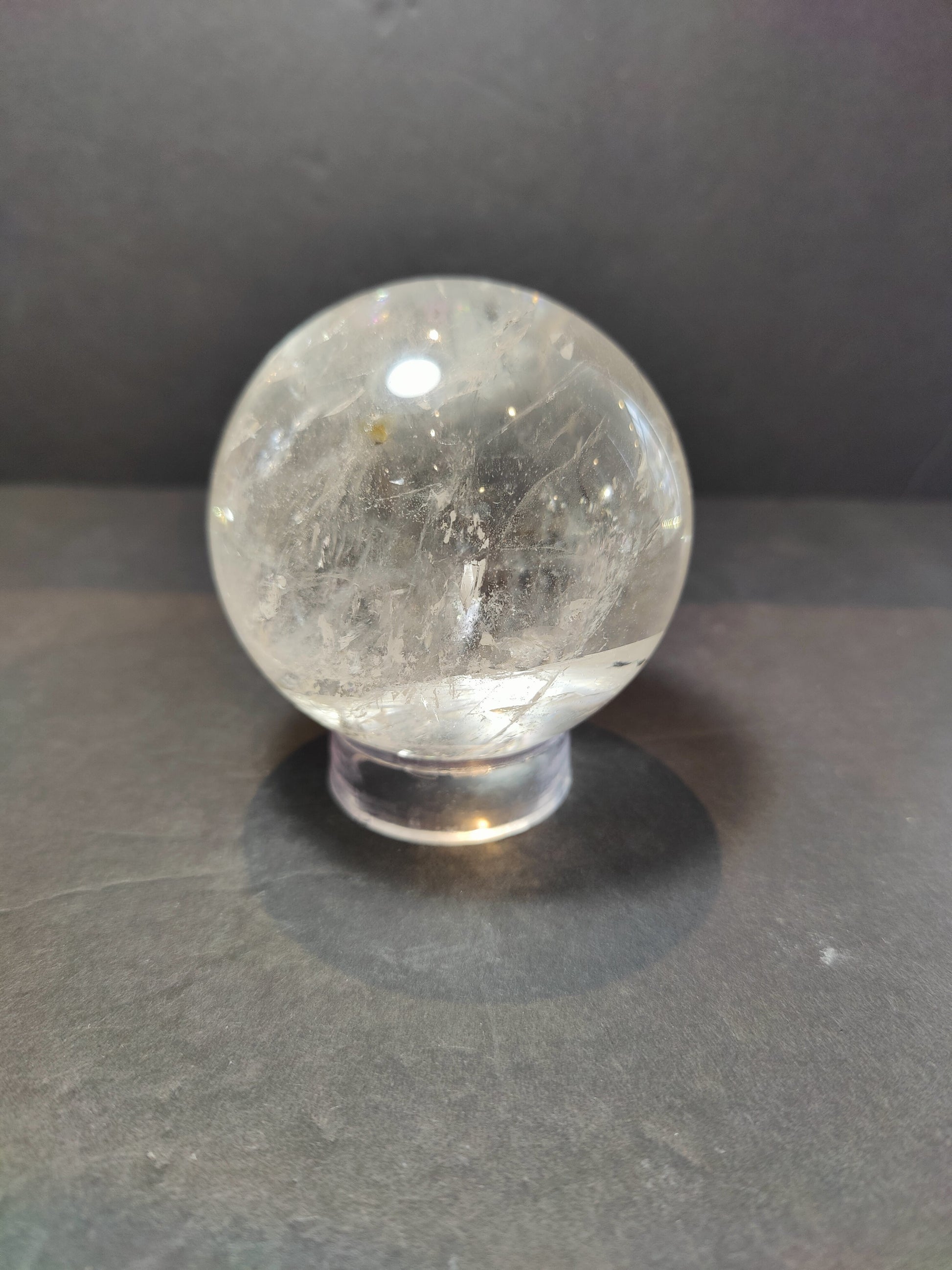 Polished clear quartz crystal sphere catching the light, with natural internal veils — view 5