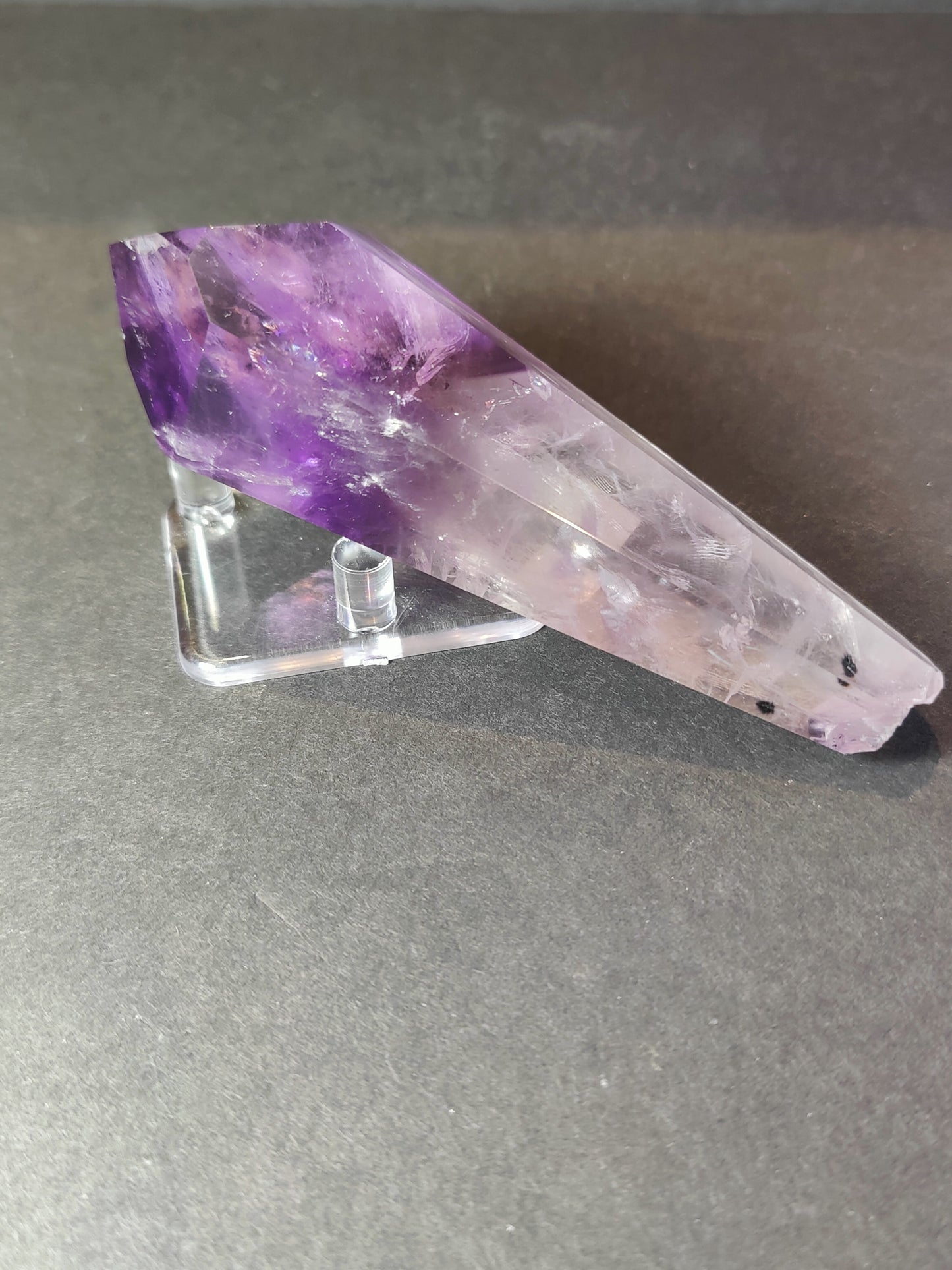 Amethyst scepter wand lying on a clear acrylic stand, showing the polished faces along its length