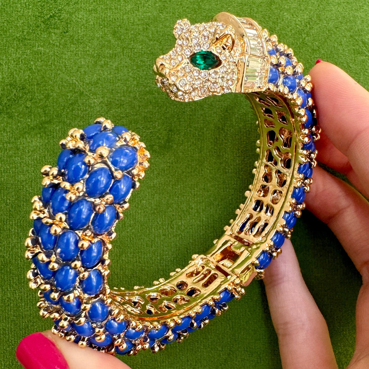The open navy blue cuff held in a hand, showing the pierced gold gallery inside the shank.