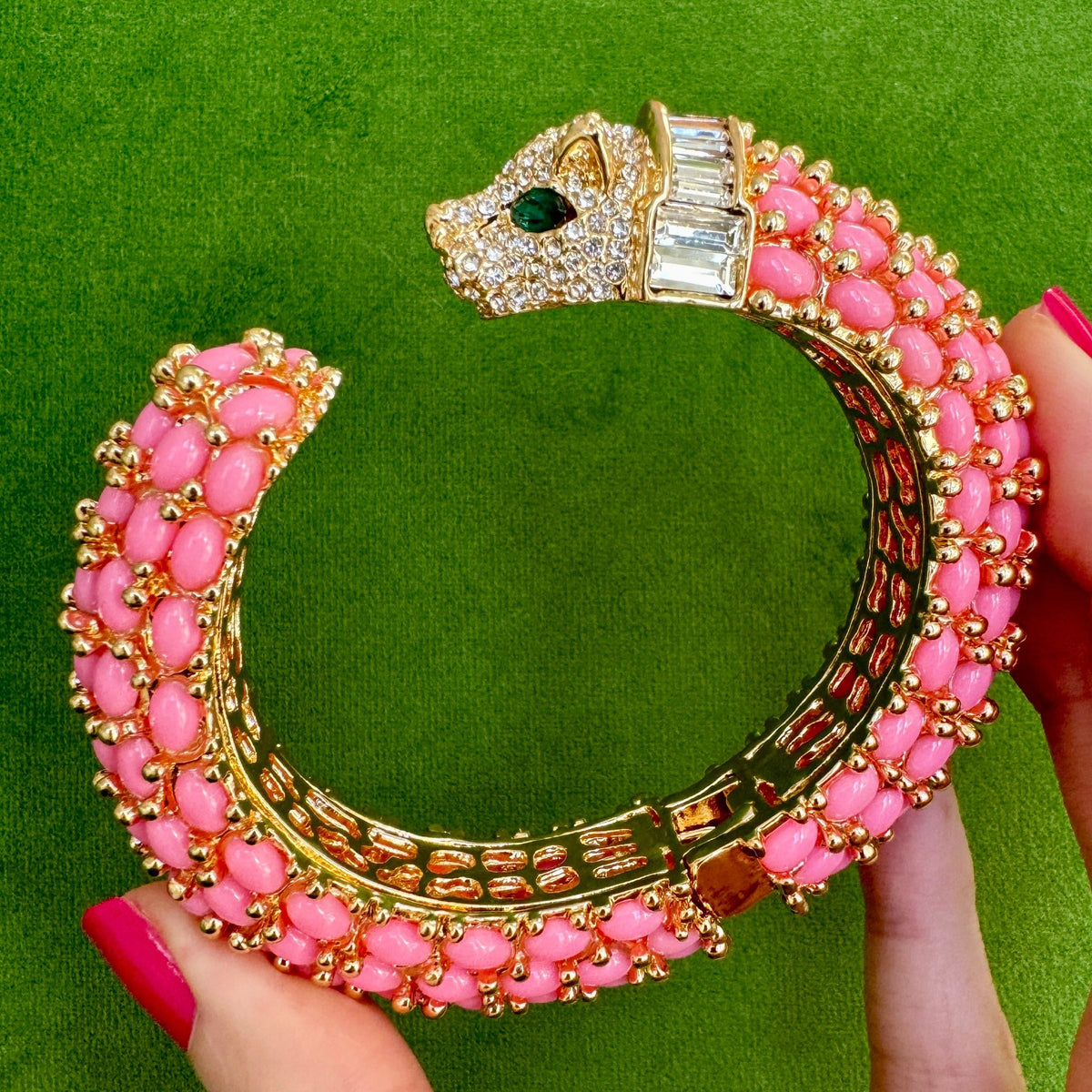 The bright pink panther cuff held open in a hand, showing the pierced gold gallery inside the shank.