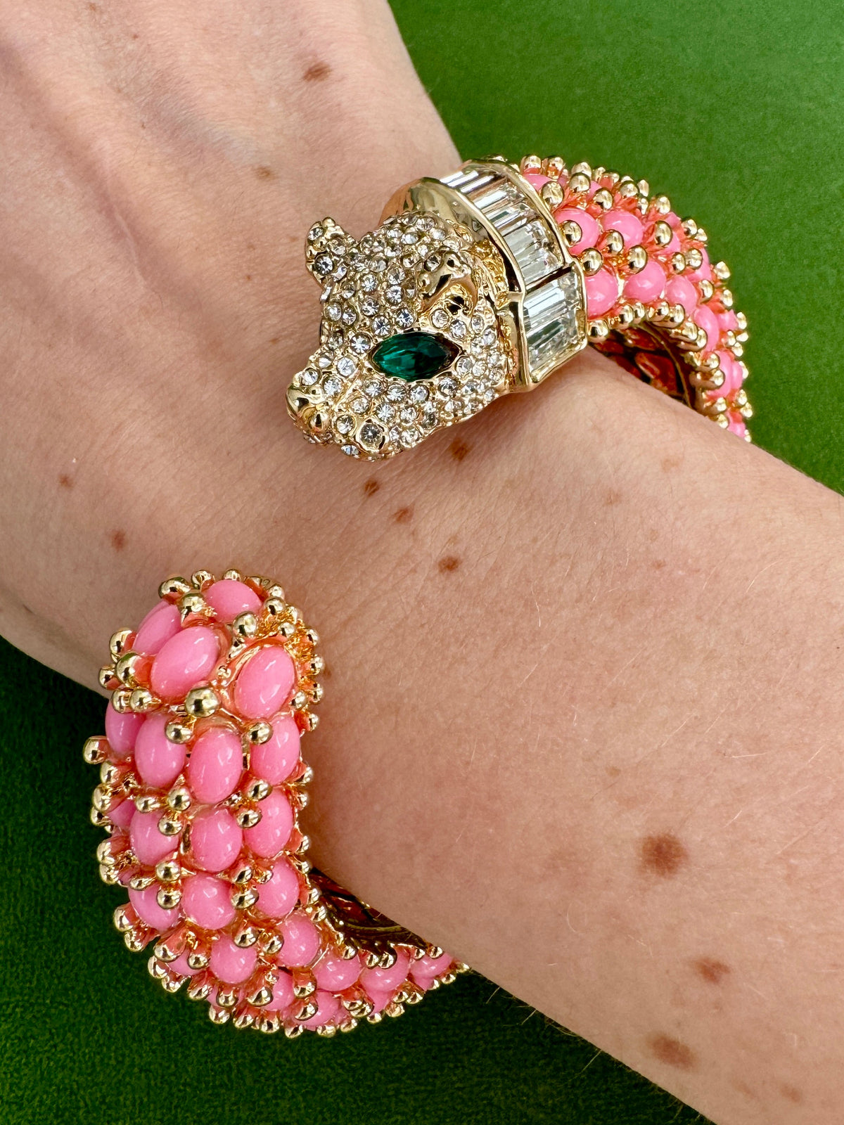 The bright pink panther cuff worn on a wrist, the pavé head with a green marquise eye.