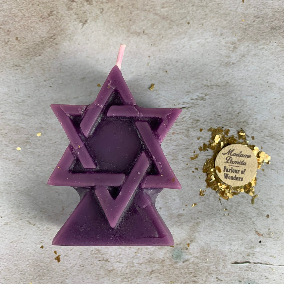 Purple beeswax Seal of Solomon hexagram candle on stone scattered with gold leaf