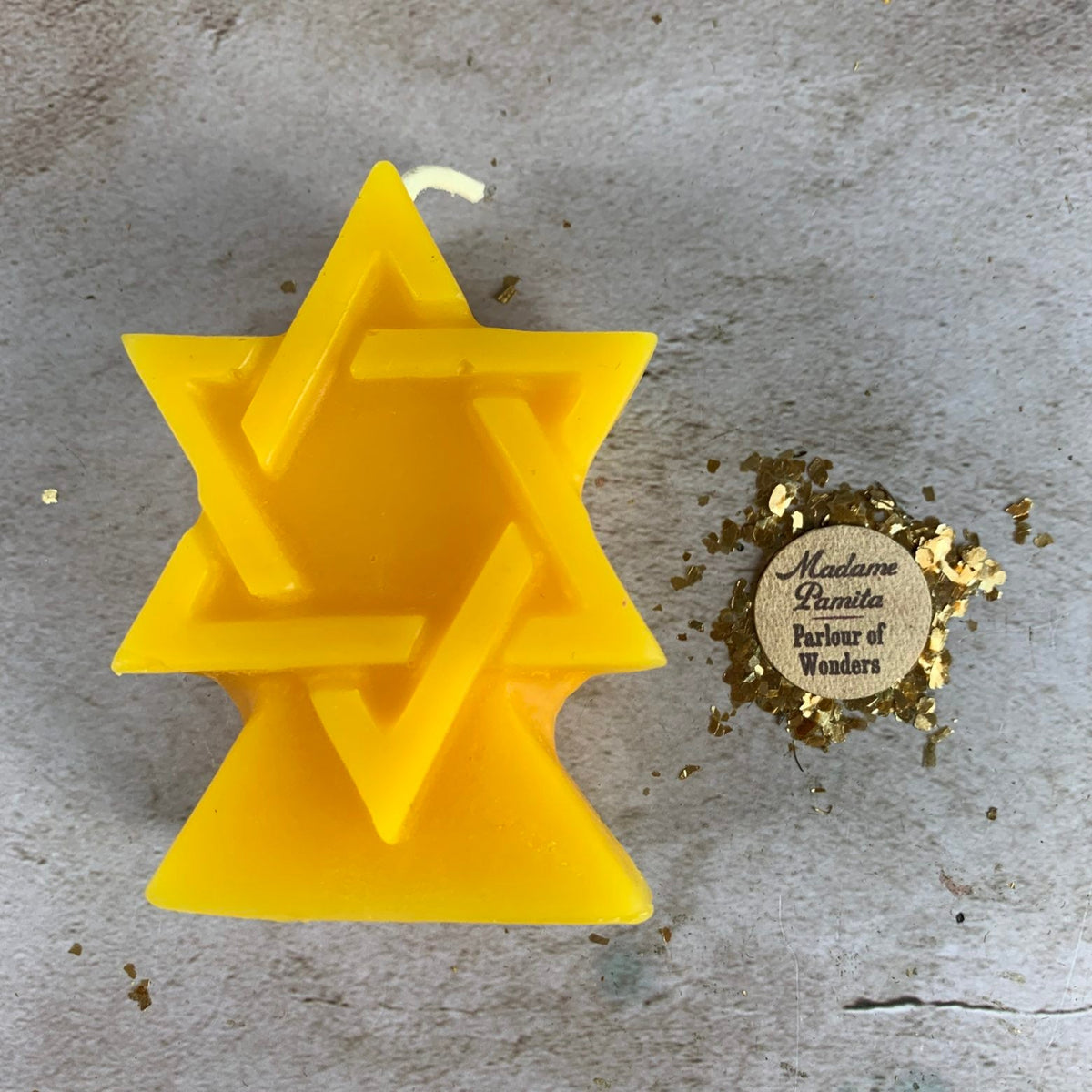 Golden yellow beeswax candle cast as the interlocking Seal of Solomon hexagram, on pale stone with gold leaf