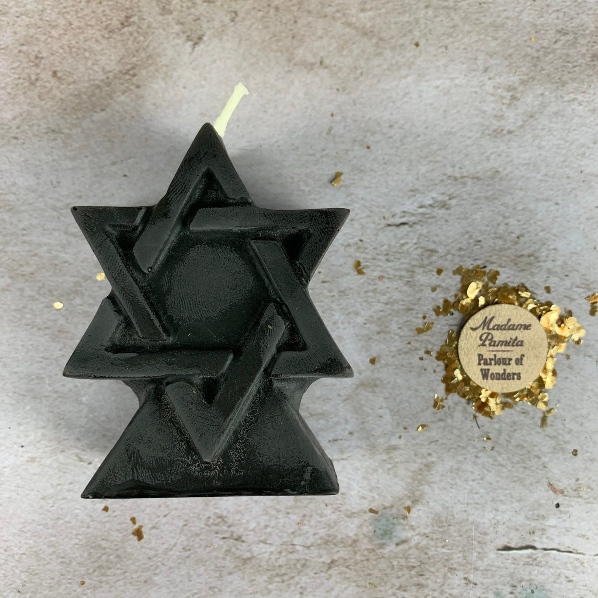 Black beeswax Seal of Solomon hexagram candle on a pale stone surface with gold flecks