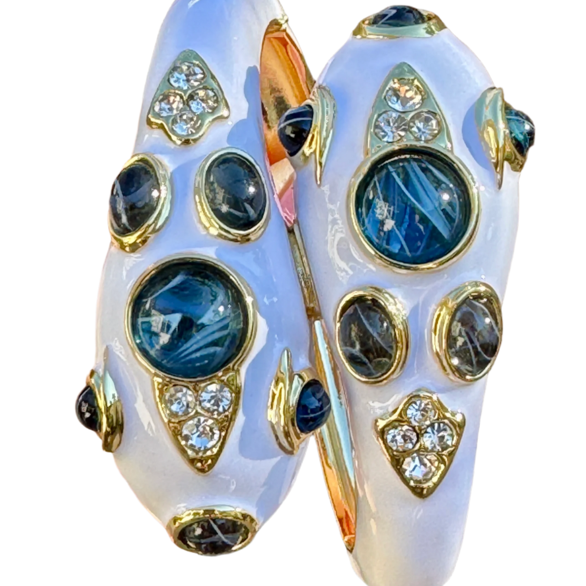 Close-up of both snake heads in white enamel, each with a large blue cabochon at the crown, smaller blue stones along the sides and clear pave set into gold-tone bezels.