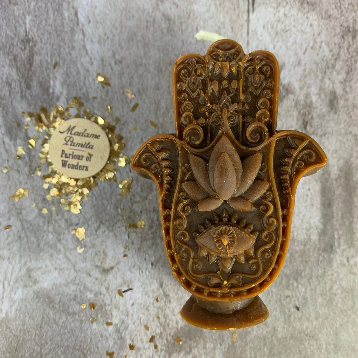 Brown Hamsa candle with darker antiquing in the recesses, showing the raised lotus and the eye beneath it.