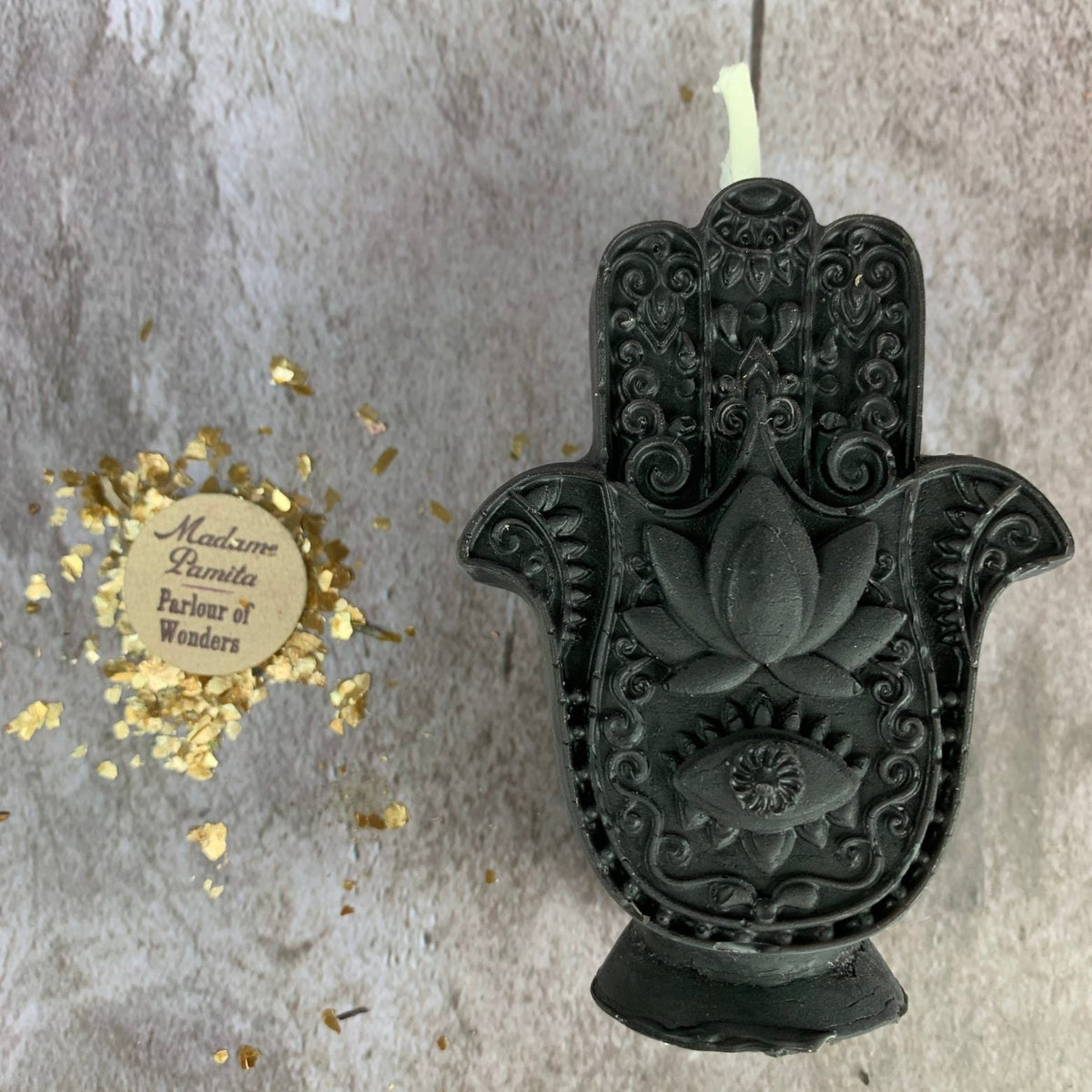 Black Hamsa candle on gray concrete, the pattern readable only in the shadows of the relief.