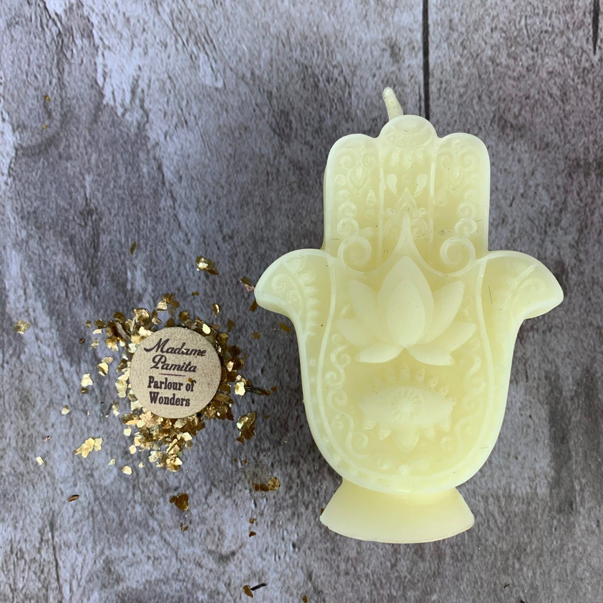 Cream-white Hamsa candle, the lotus and filigree crisply molded, beside the Parlour of Wonders label and gold flakes.