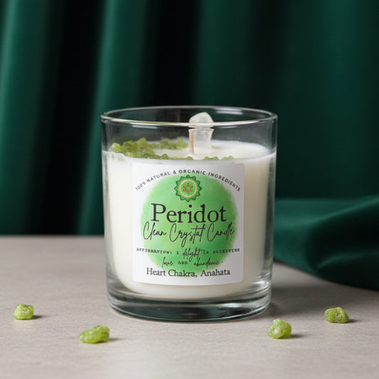 Peridot crystal candle in its clear glass tumbler on gray stone against a dark green drape, peridot chips beside it