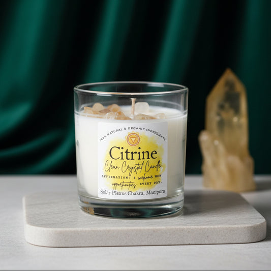 Citrine crystal candle in a clear glass tumbler on a pale stone tile, a large citrine point beside it and green velvet behind