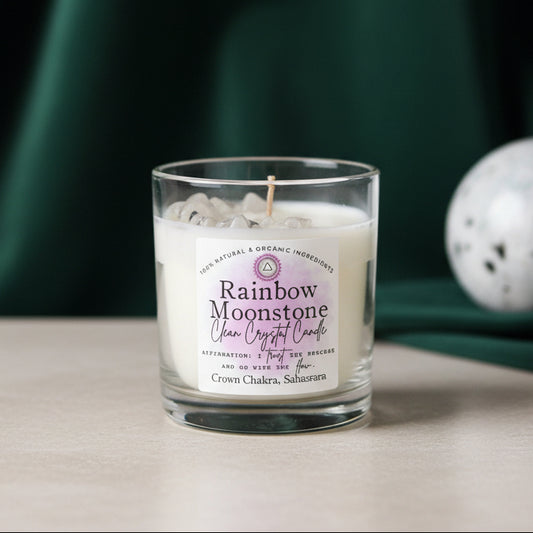 Rainbow Moonstone crystal candle in a clear glass tumbler on a wooden surface, dark green velvet draped behind