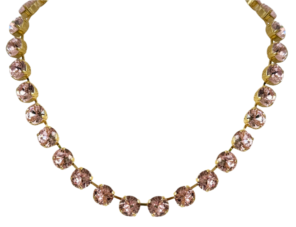 Close-up of the pink crystal necklace on black, the round stones held in gold-tone claw settings.