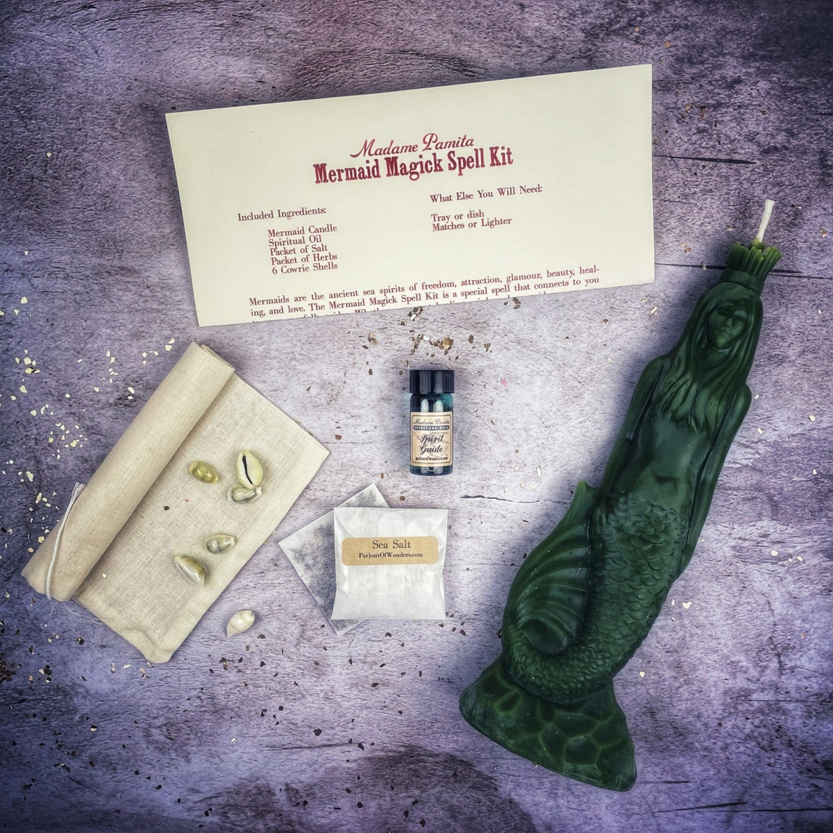 Dark green mermaid candle with the kit's card, oil, salt sachet, linen bag and shells.