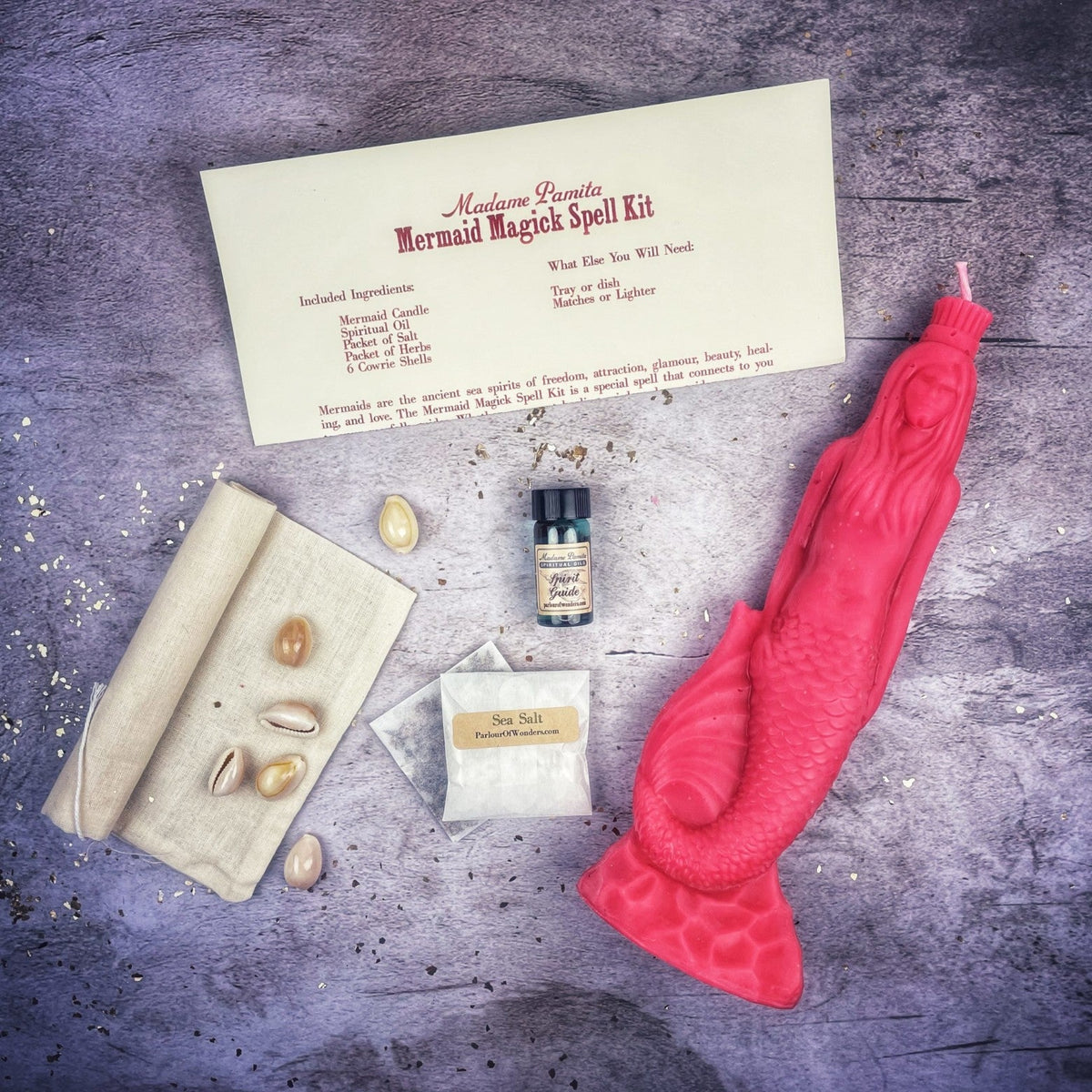 Pink mermaid candle with the full kit laid out around it, cowrie shells in cream and gold.