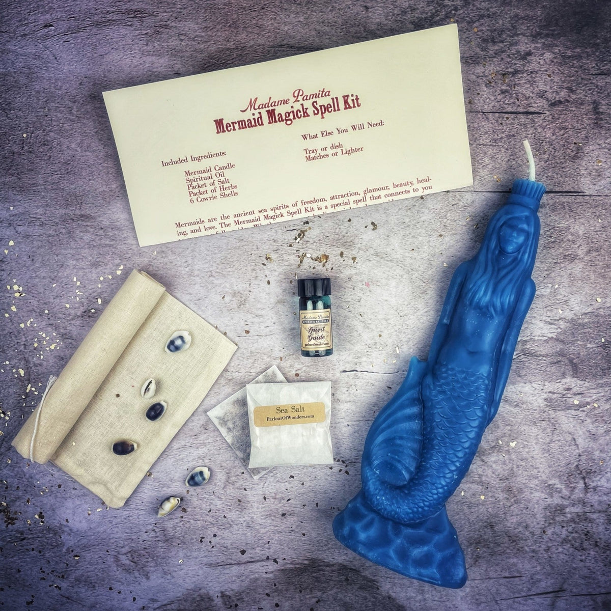 The same kit with a bright blue mermaid candle, laid out on gray stone.