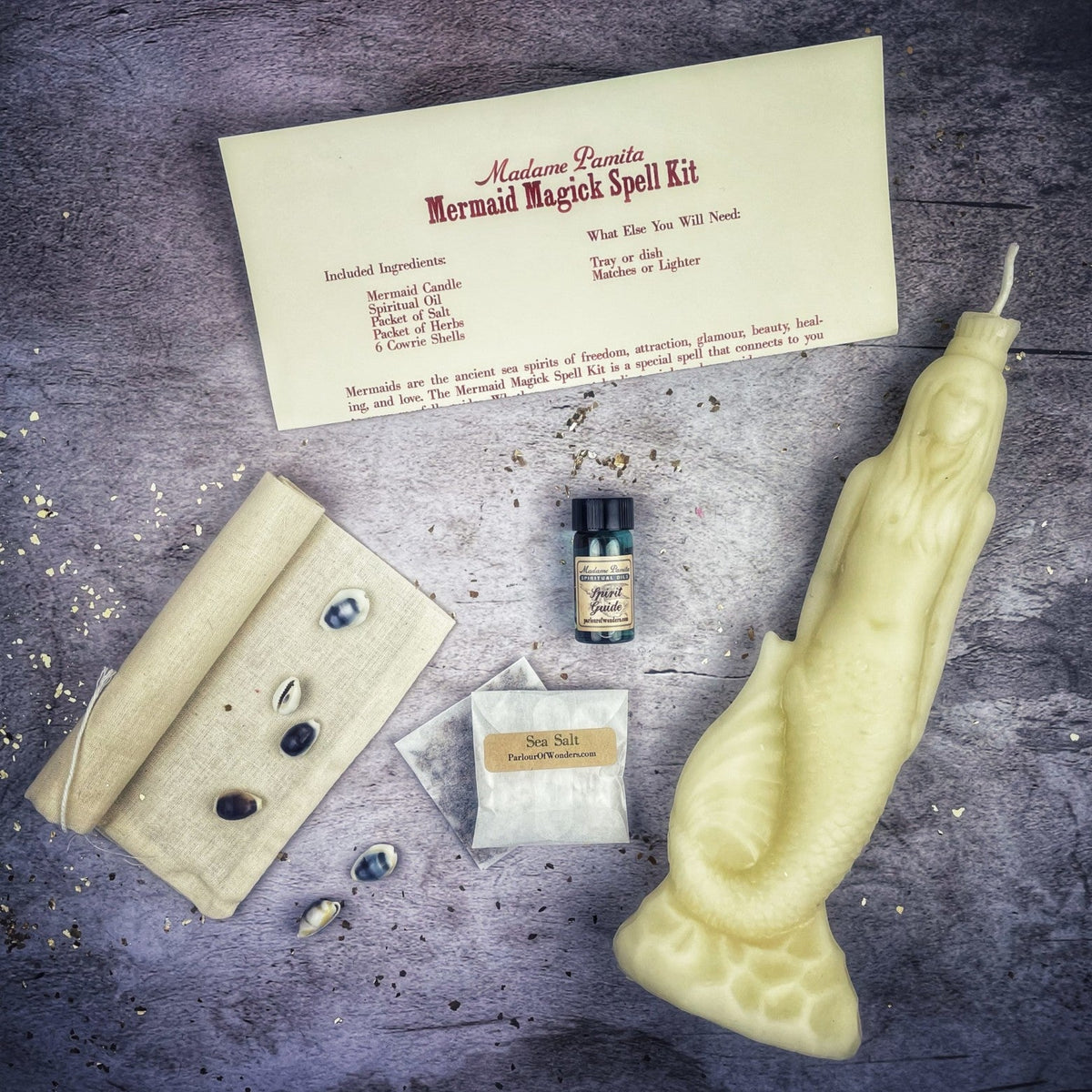 Cream-white mermaid candle with the kit's card, oil bottle, salt sachet, linen bag and cowrie shells.