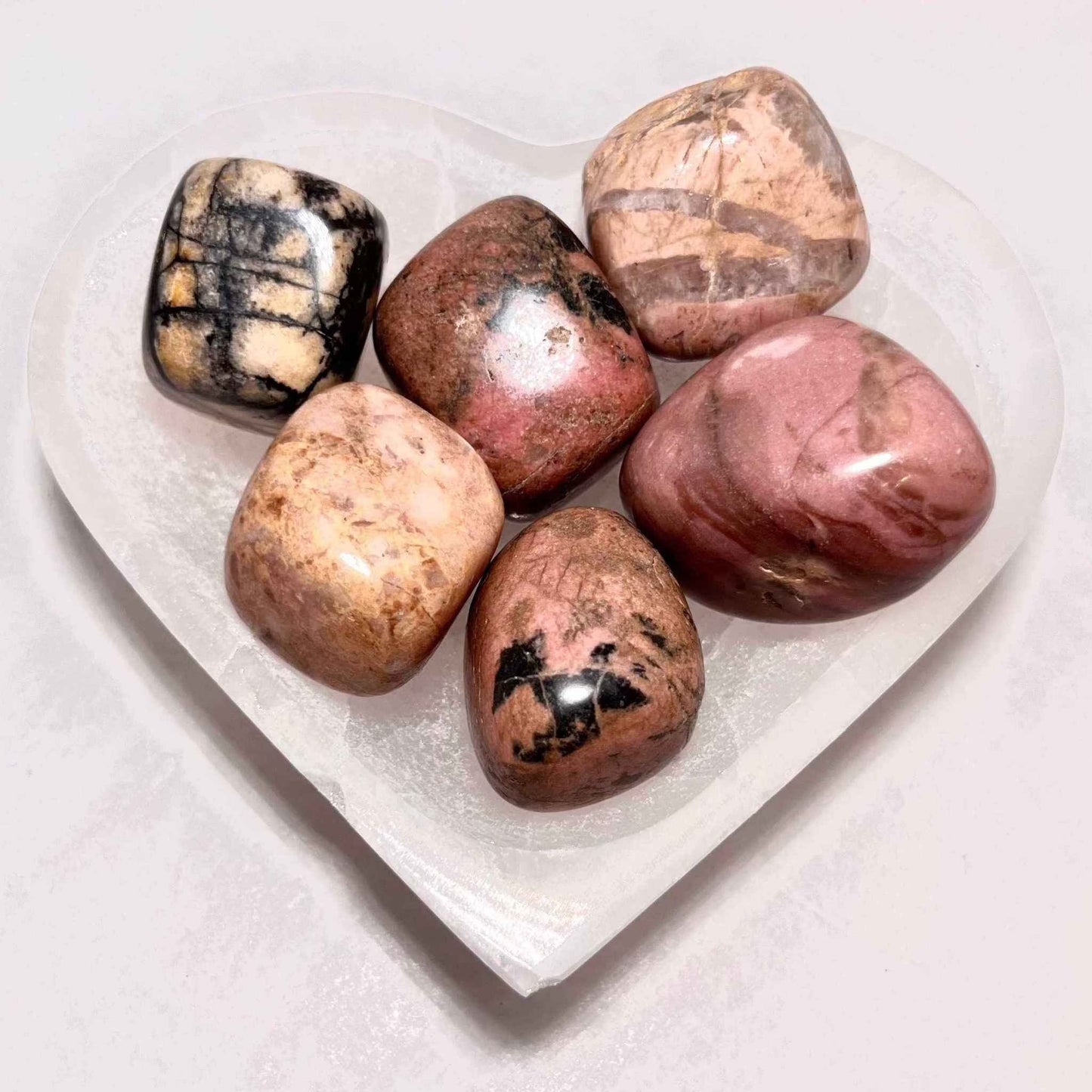 A smooth rhodonite pocket stone on a plain background.