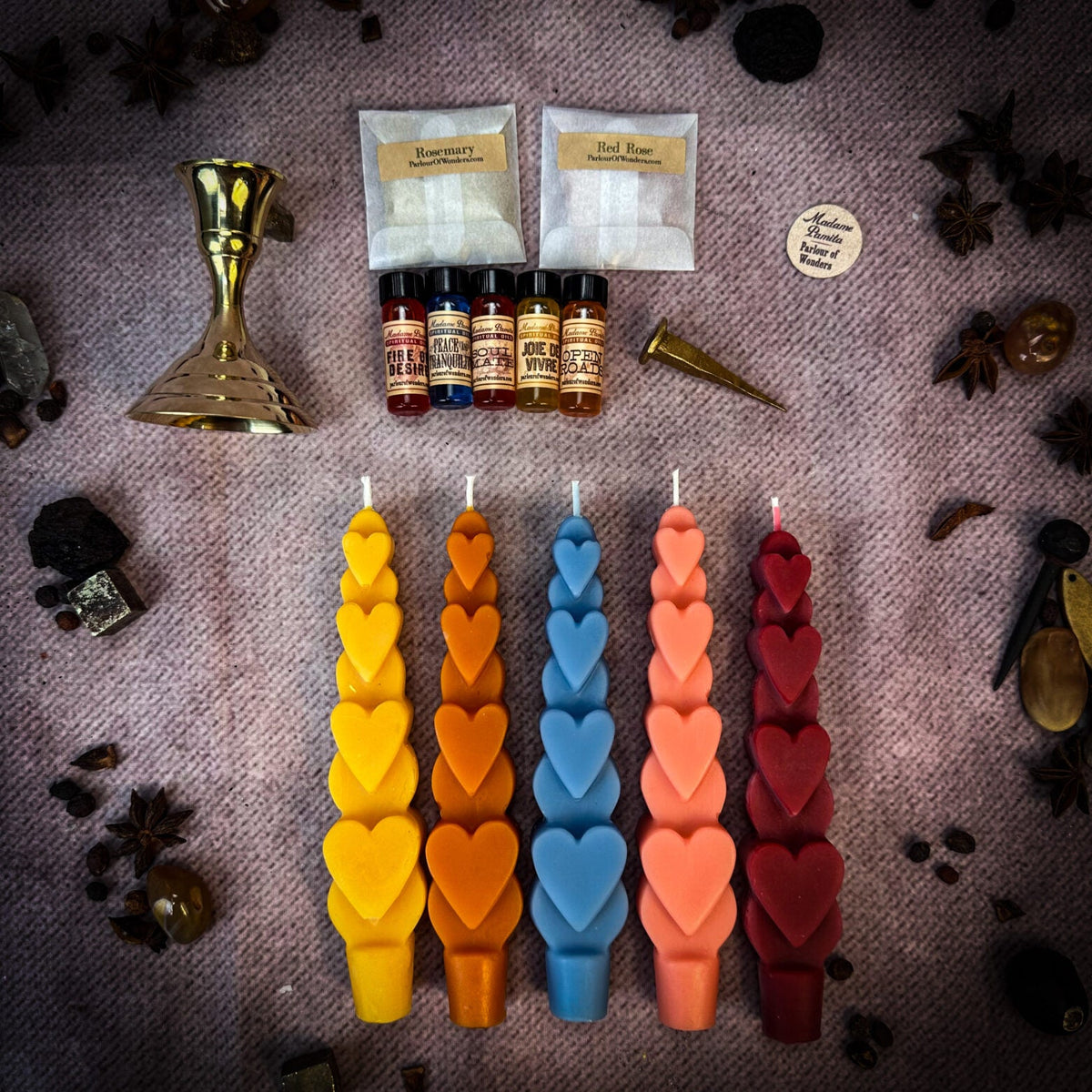 Five heart taper candles in yellow, orange, blue, pink and dark red with the brass holder, oil vials, two herb sachets and a wooden Parlour of Wonders token