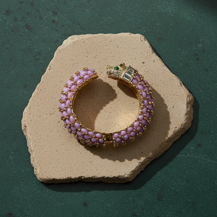 Lavender panther cuff on a pale stone slab, the open shank covered in rows of lavender oval cabochons and gold beads, with a pavé-set panther head at one end.