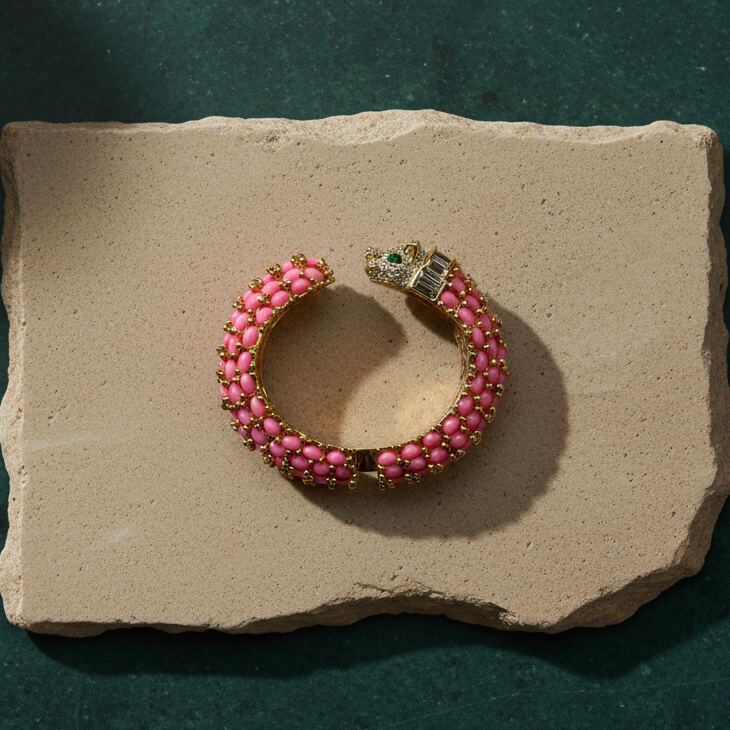 Bright pink panther cuff on a pale stone slab, rows of pink oval cabochons with gold beading and a pavé-set panther head.