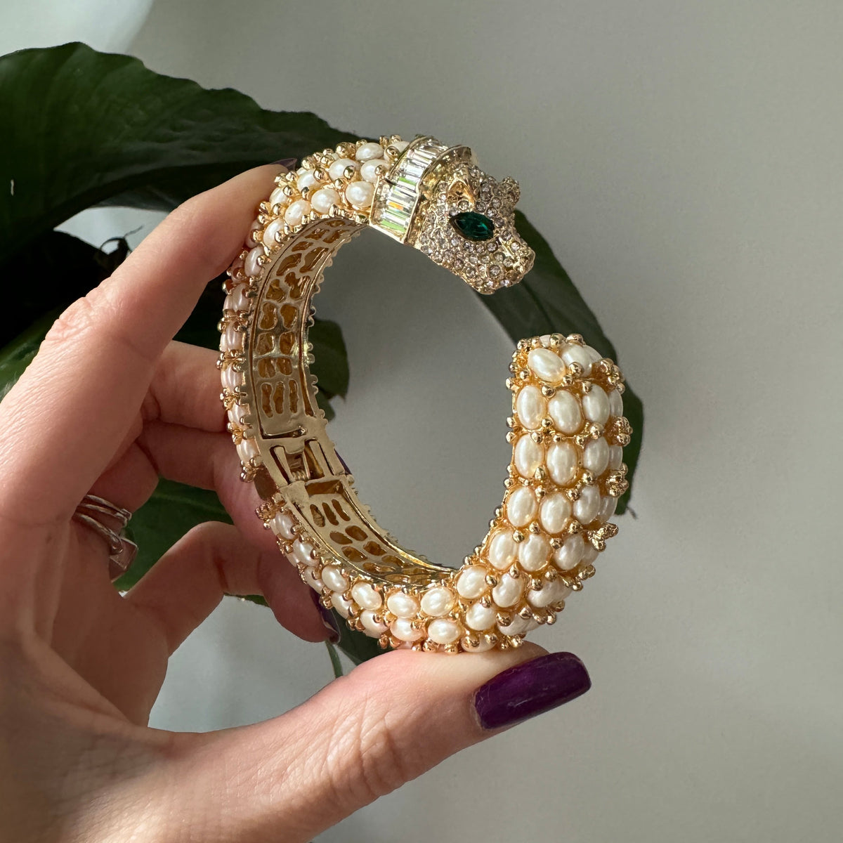 The open pearl cuff held in a hand, showing the pierced gold gallery inside the shank.