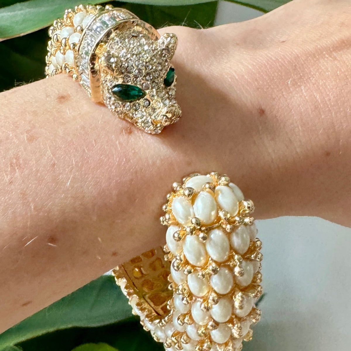 The pearl panther cuff worn on a wrist against green leaves, the pavé head facing the pearl-set tail.
