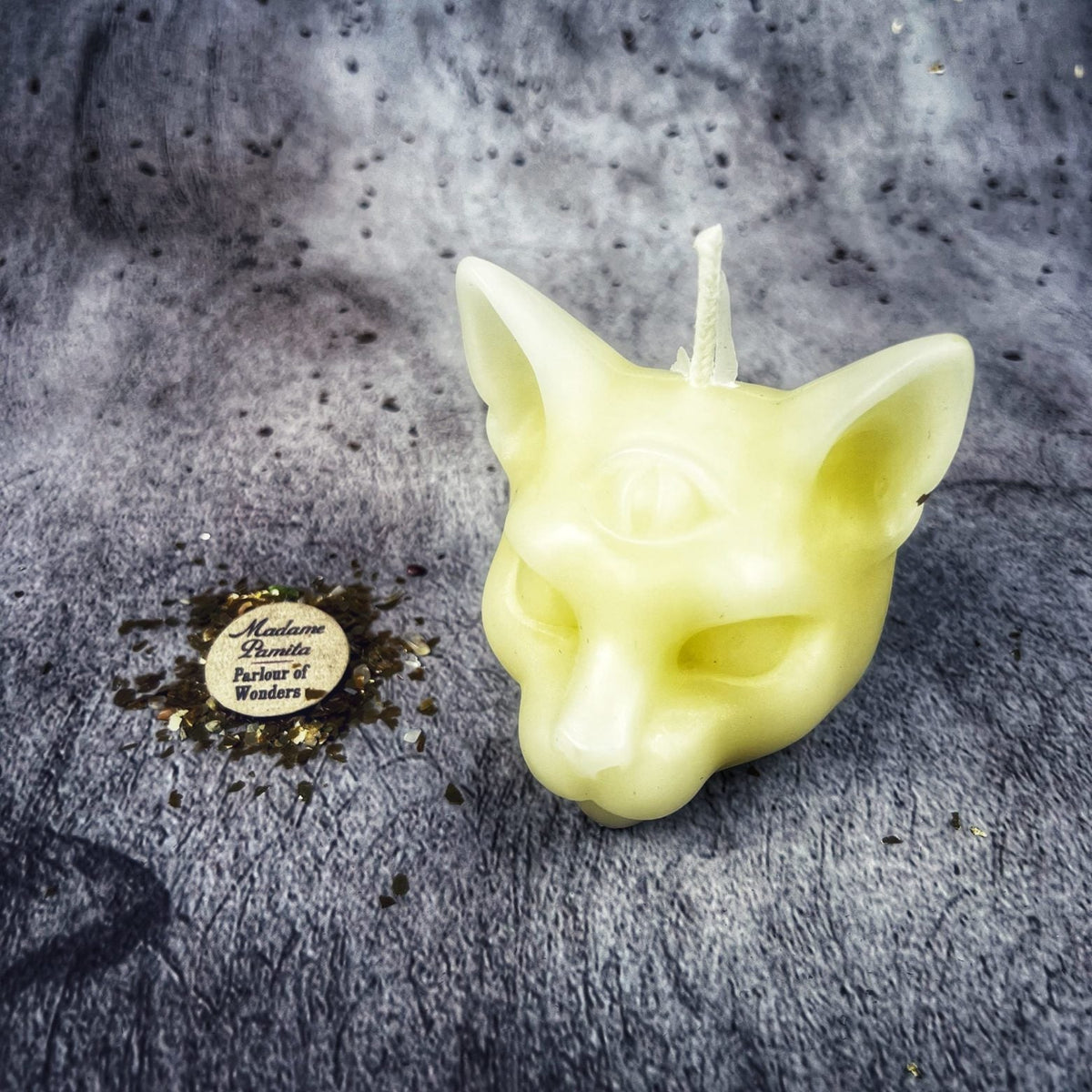 Pale yellow cat head candle beside the Madame Pamita label and gold leaf on gray fur.