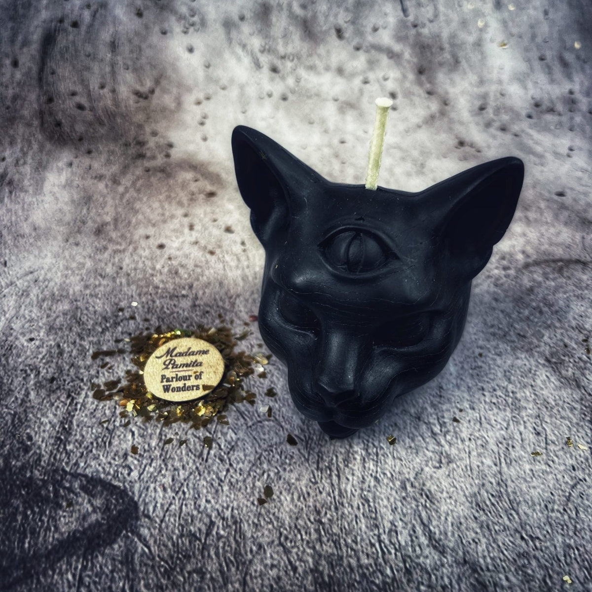 Black cat head candle on gray stone beside the Parlour of Wonders label.