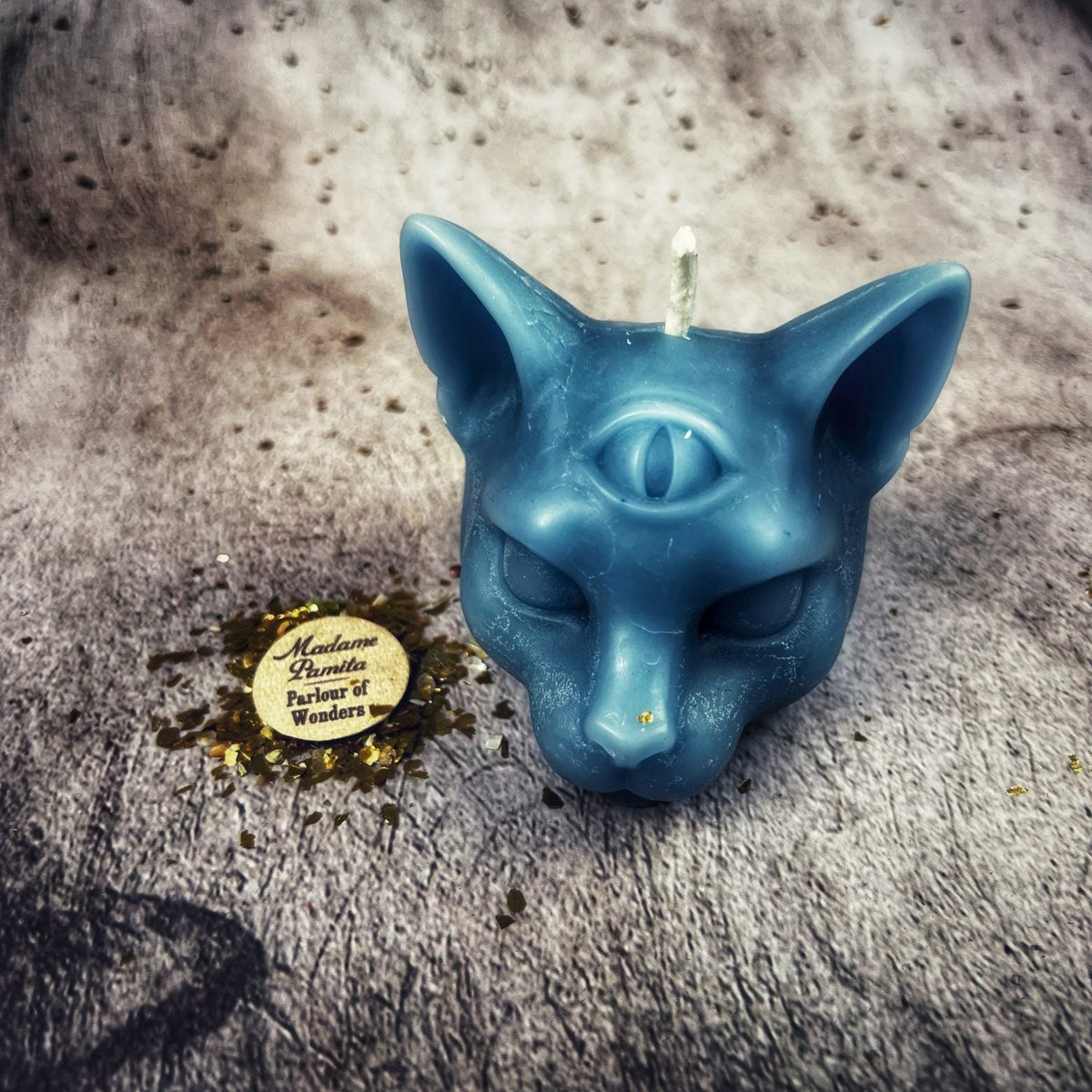 Teal-blue cat head candle on gray fur with gold leaf beside it.