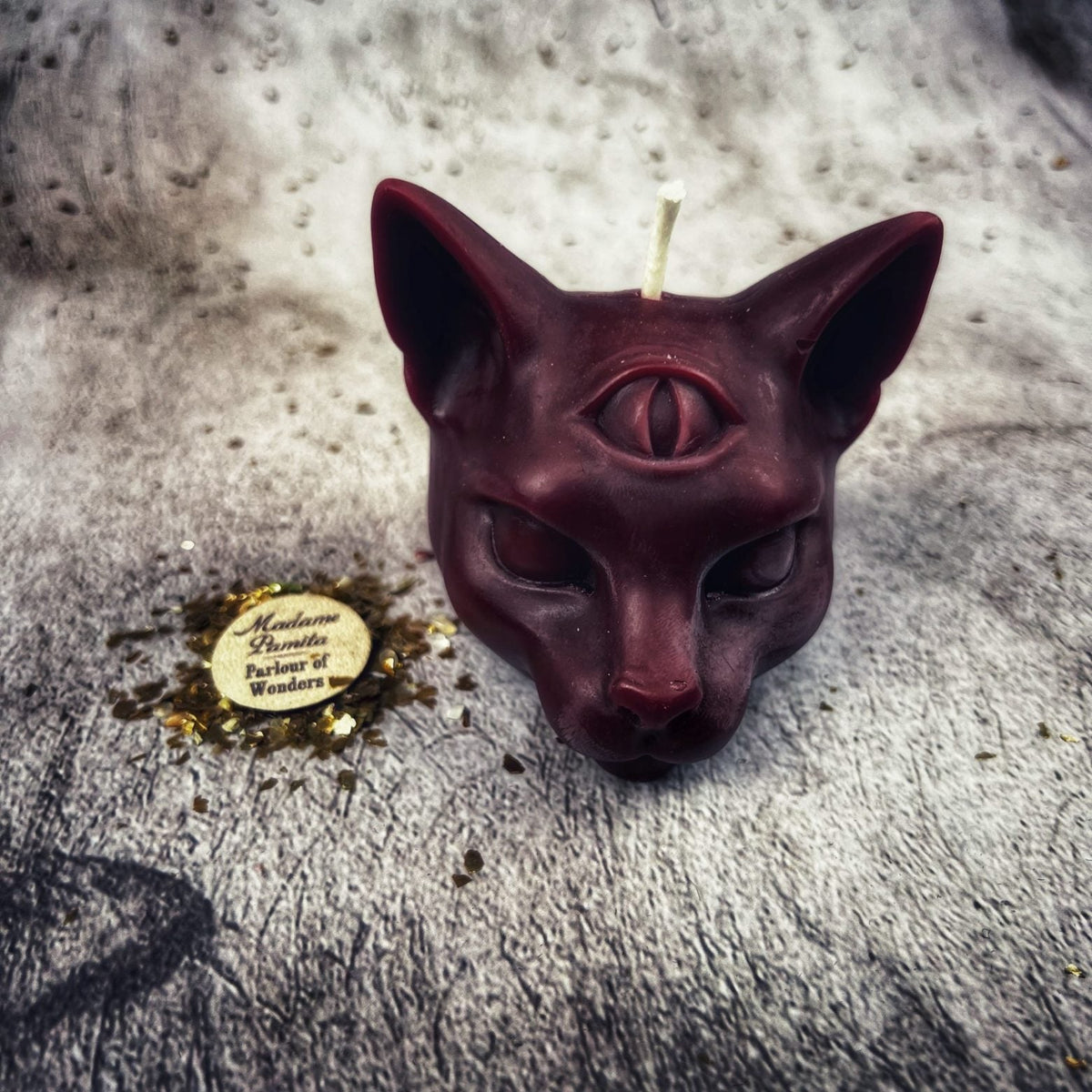 Deep wine-red cat head candle, ears sharp and the muzzle catching the light.