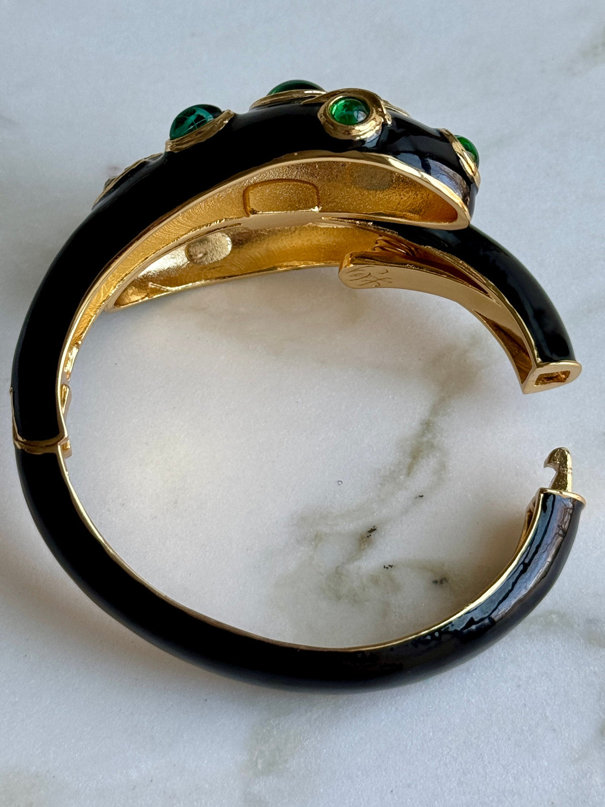 Underside of the black snake cuff on marble, showing the polished gold interior and the hinge in the shank.
