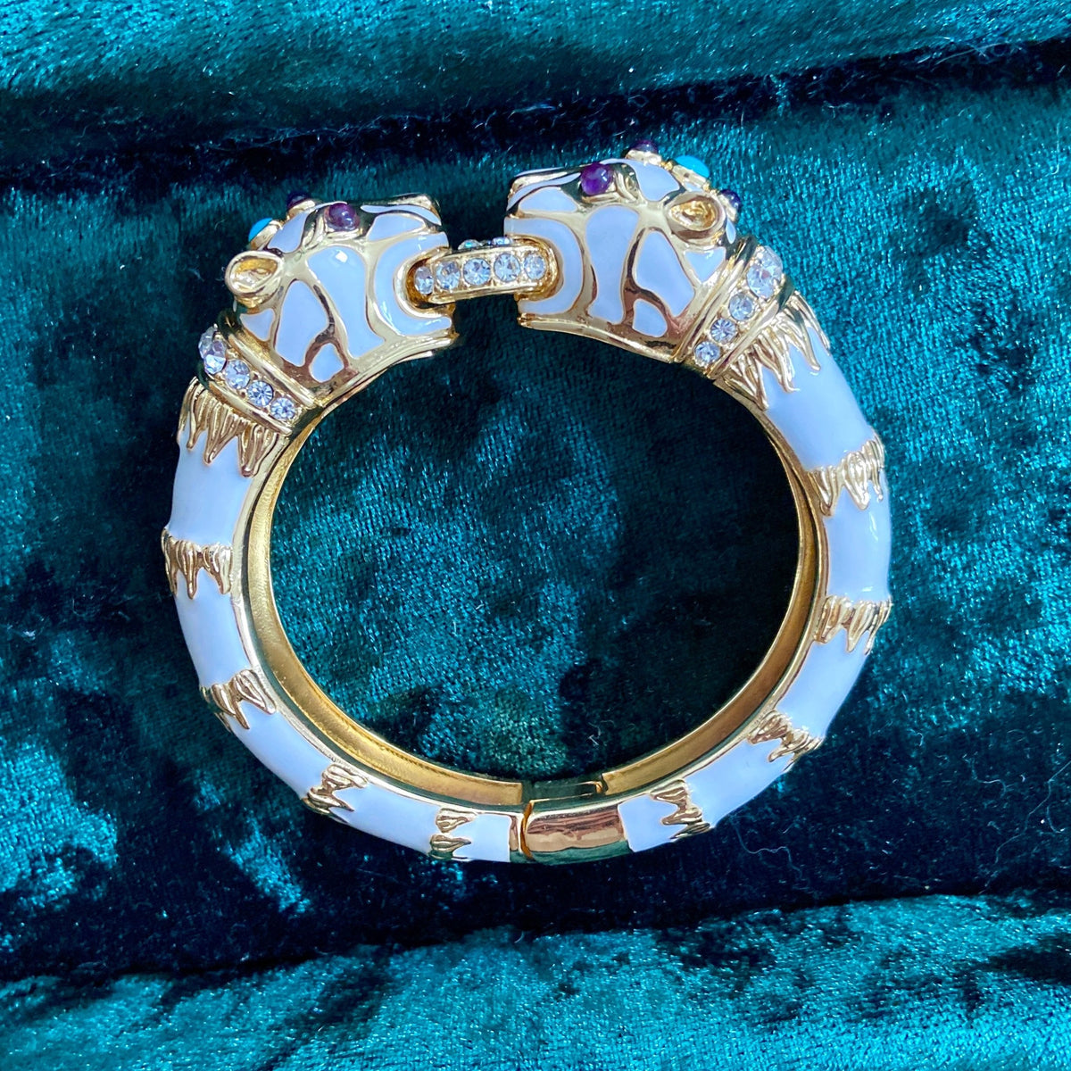 The white enamel panther cuff photographed from above on teal velvet.