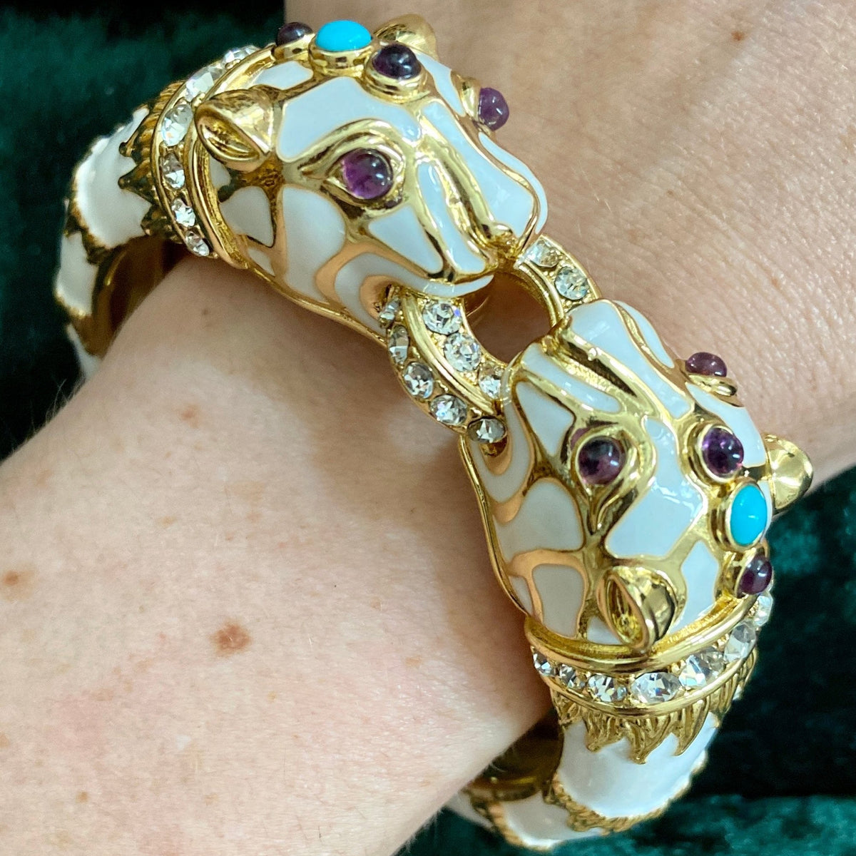 The white panther cuff worn on a wrist against dark green velvet, both heads visible along the top.