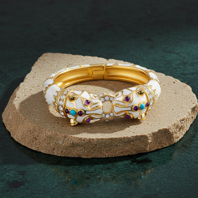 White enamel double panther cuff on a pale stone slab, two panther heads facing each other across a pavé-set link, with purple and turquoise-blue cabochons.