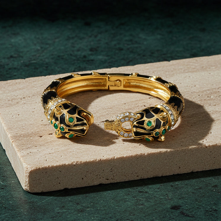 Black enamel double panther cuff on a pale stone slab, gold openwork striping over black enamel with green cabochon eyes and pavé-set collars.