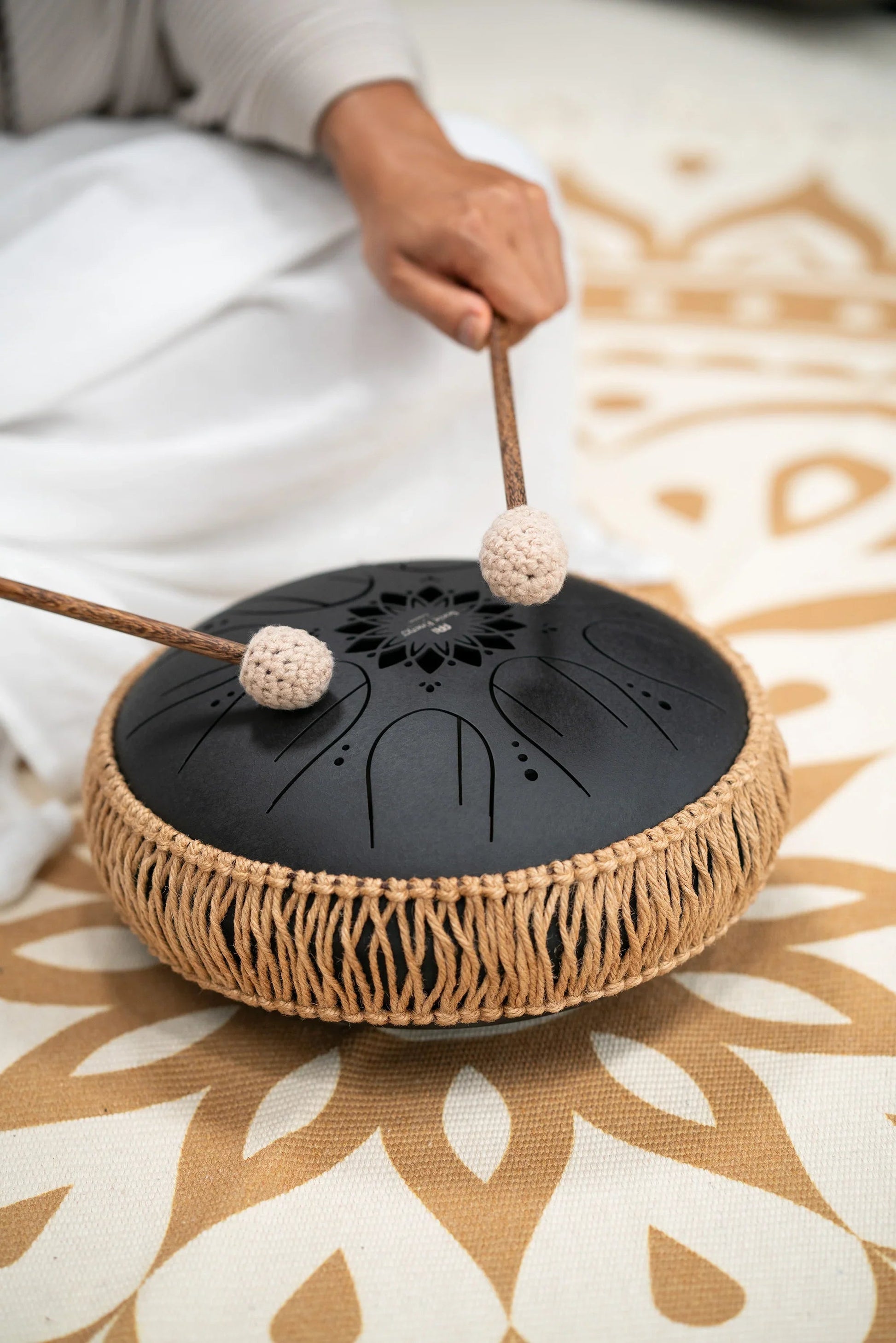 Black 10-inch steel tongue drum shown in a warm, softly lit styled scene.