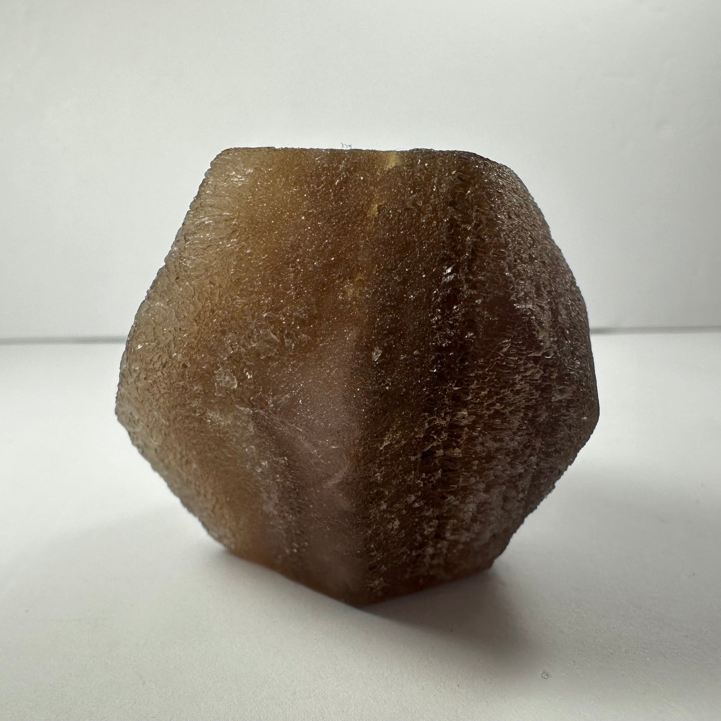 Polished fluorite dodecahedron with twelve pentagonal faces in banded green and purple, held in daylight — view 3