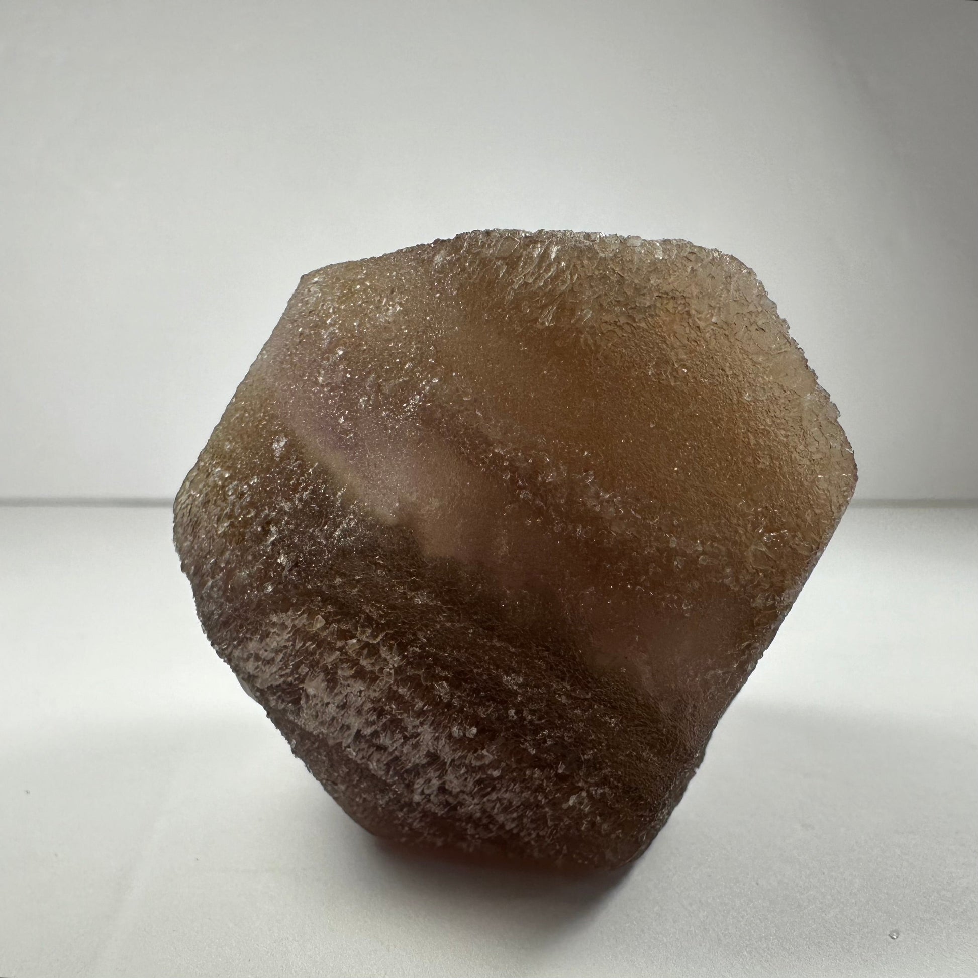 Polished fluorite dodecahedron with twelve pentagonal faces in banded green and purple, held in daylight — view 4