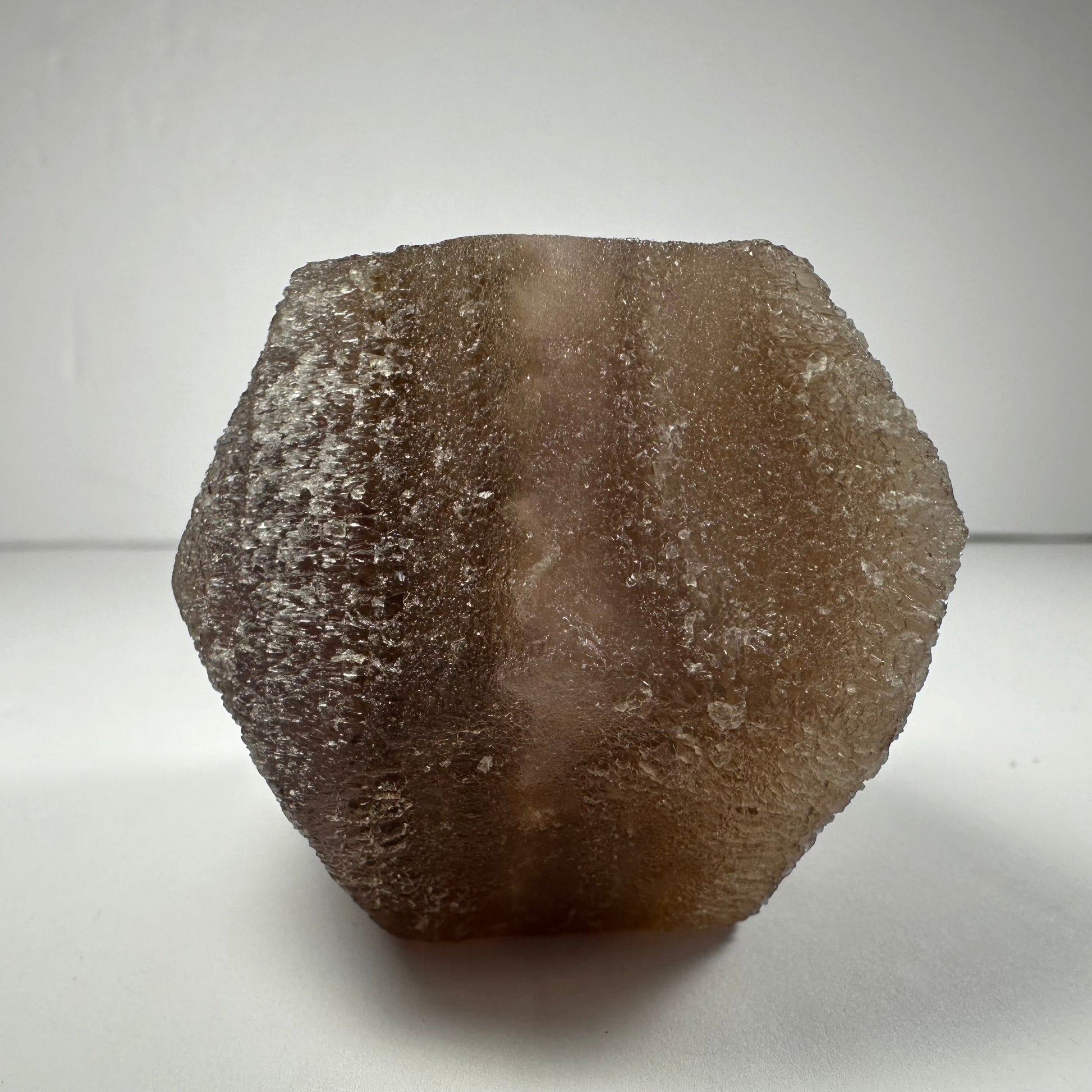 Polished fluorite dodecahedron with twelve pentagonal faces in banded green and purple, held in daylight — view 5