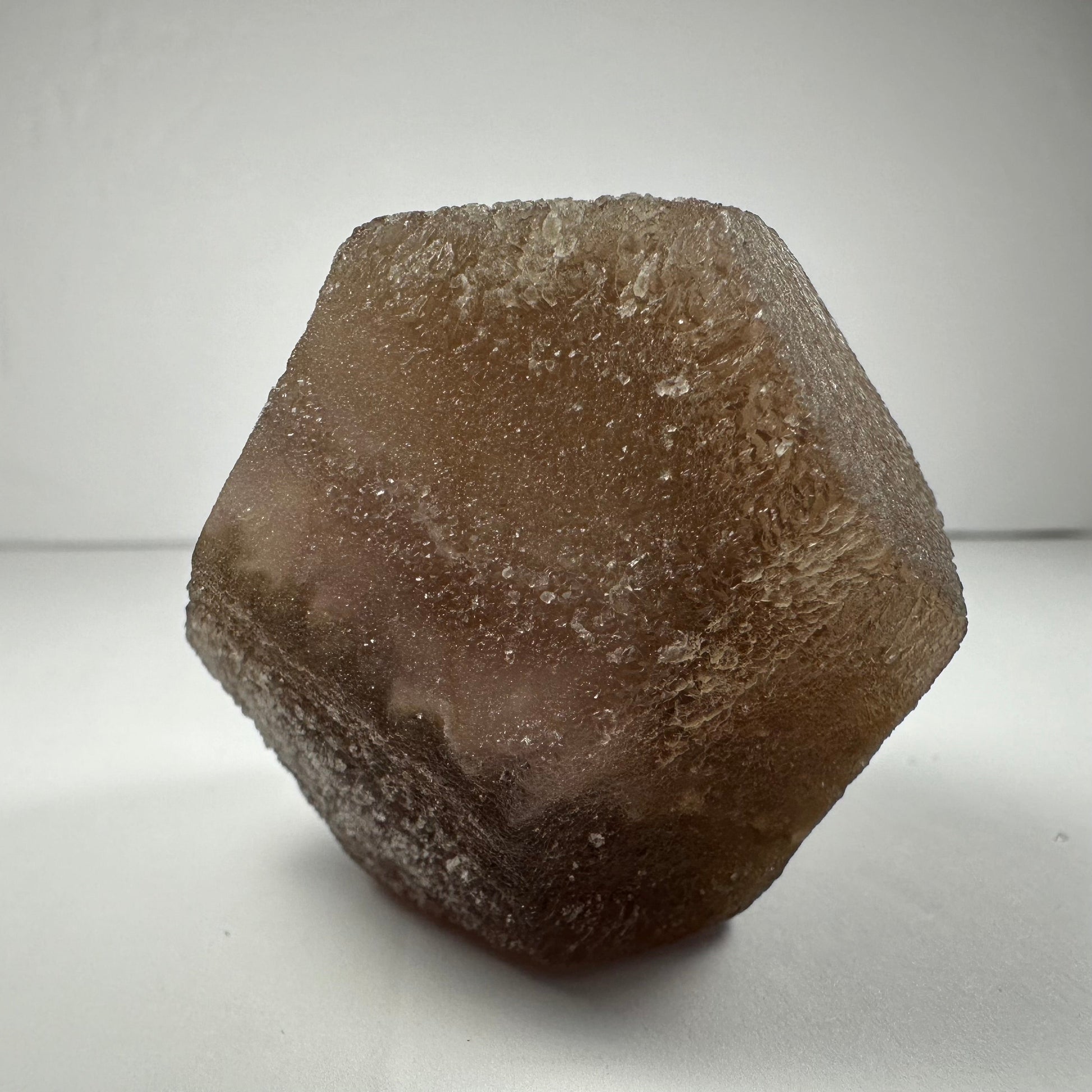 Polished fluorite dodecahedron with twelve pentagonal faces in banded green and purple, held in daylight — view 2