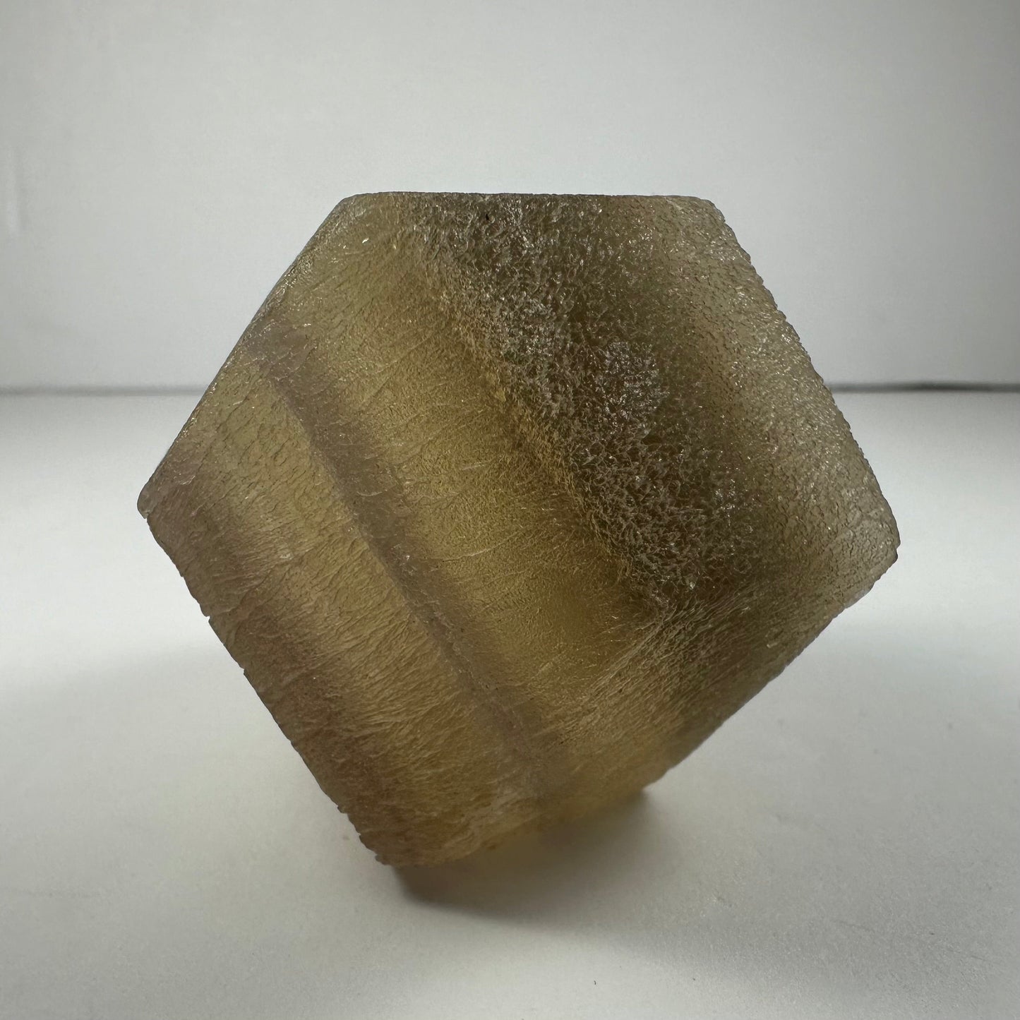 Polished fluorite dodecahedron with twelve pentagonal faces in banded green and purple, held in daylight
