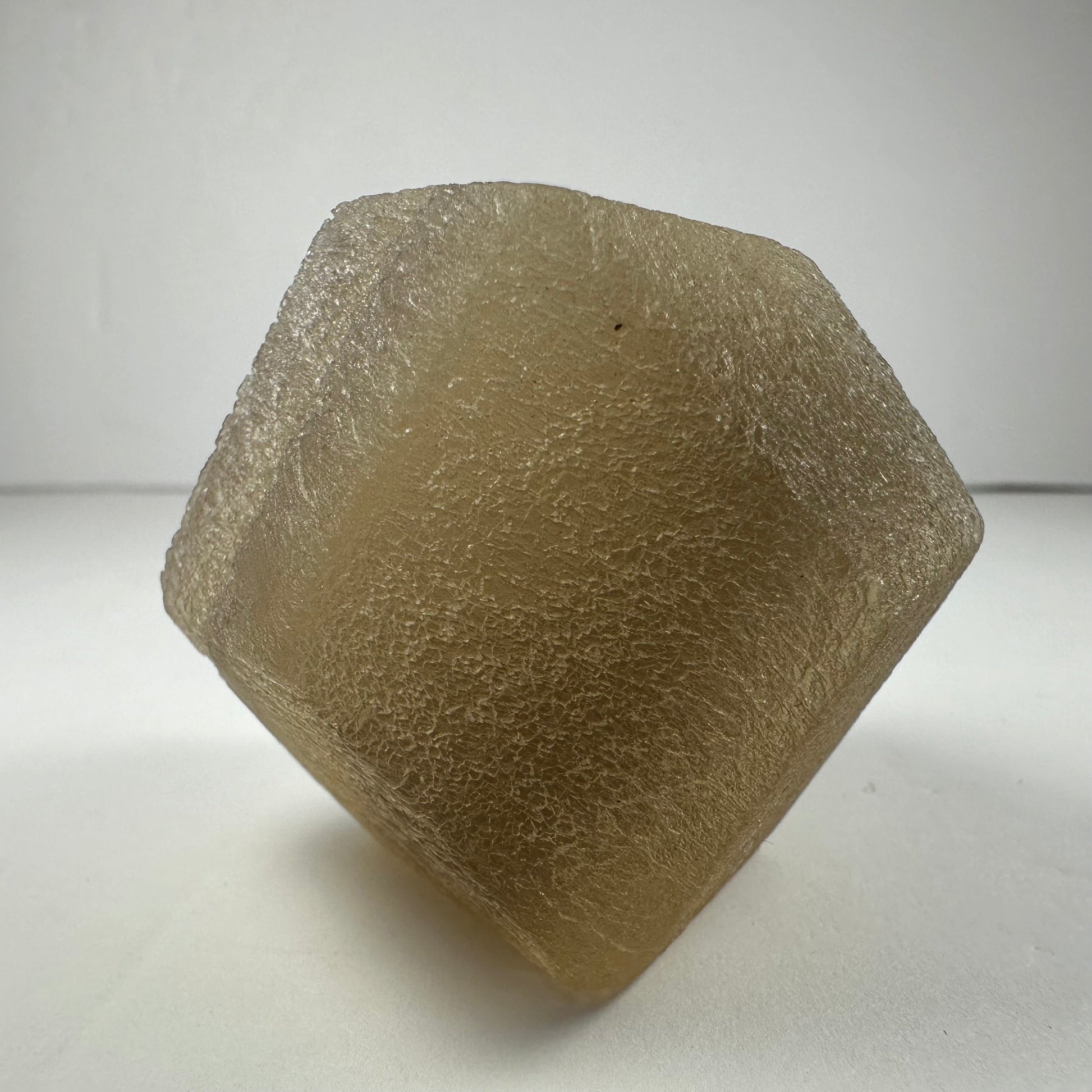 Polished fluorite dodecahedron with twelve pentagonal faces in banded green and purple, held in daylight — view 6