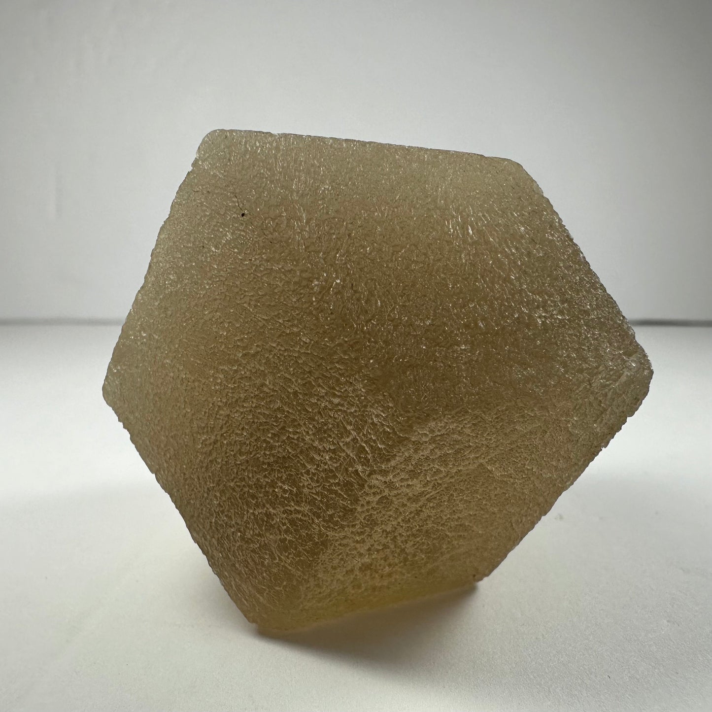 Polished fluorite dodecahedron with twelve pentagonal faces in banded green and purple, held in daylight — view 7