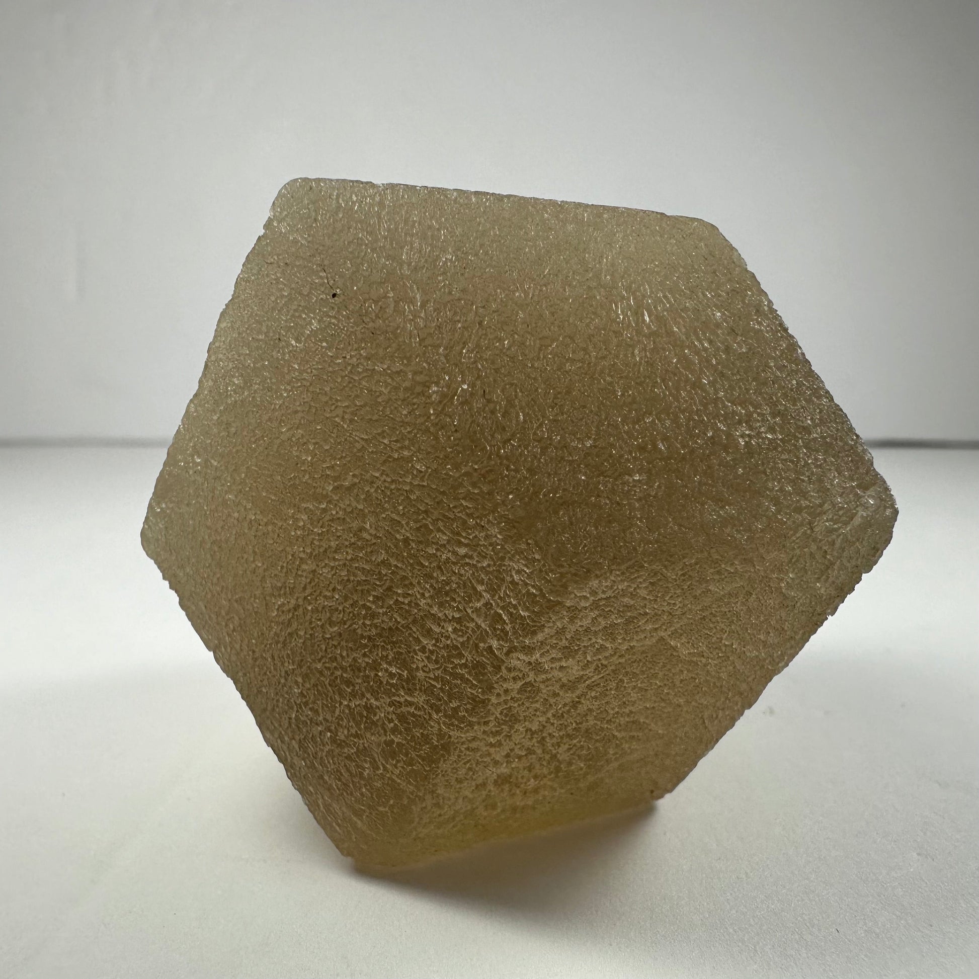 Polished fluorite dodecahedron with twelve pentagonal faces in banded green and purple, held in daylight — view 7