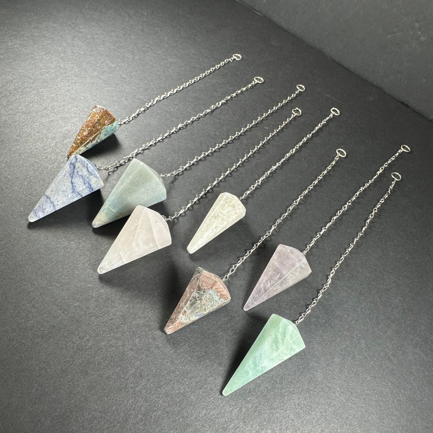 Faceted stone pendulum hanging from a seven-inch metal chain against a dark background — view 3