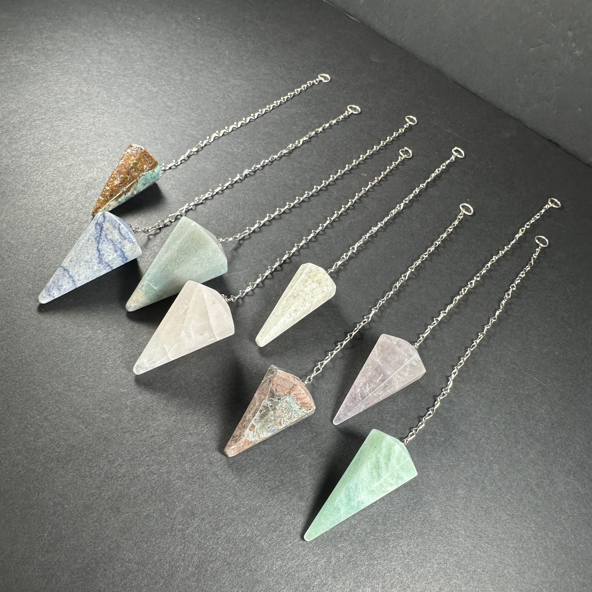 Faceted stone pendulum hanging from a seven-inch metal chain against a dark background — view 3