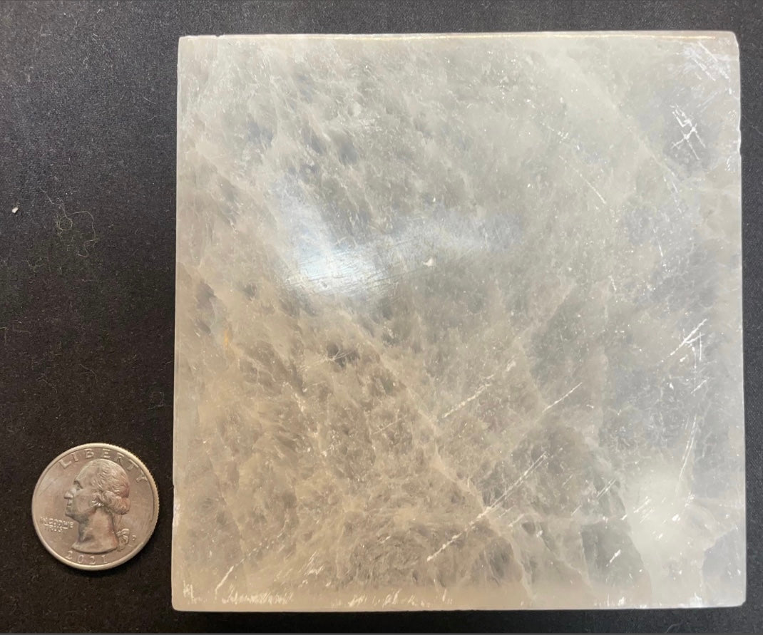 Round polished white selenite charging plate, 10cm across, translucent banded stone on a dark surface — view 3