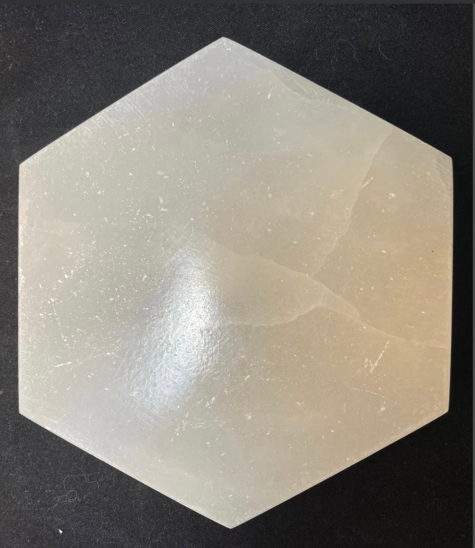 Round polished white selenite charging plate, 10cm across, translucent banded stone on a dark surface — view 2