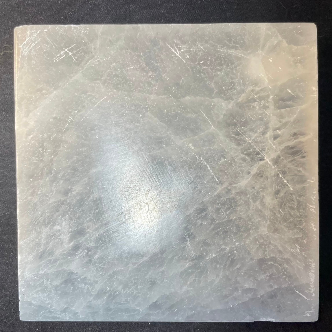 Round polished white selenite charging plate, 10cm across, translucent banded stone on a dark surface