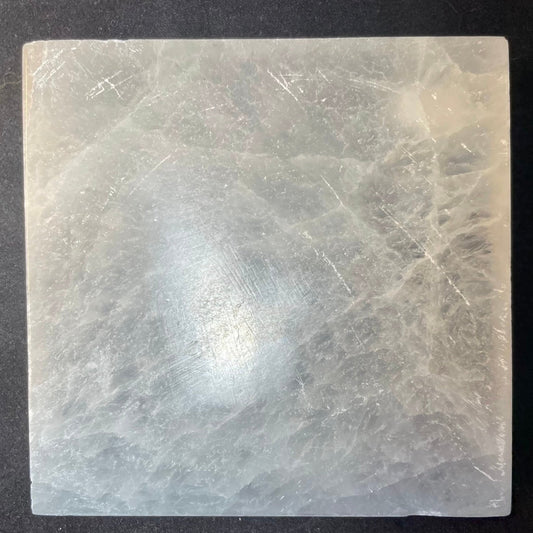 Round polished white selenite charging plate, 10cm across, translucent banded stone on a dark surface